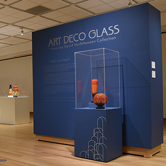 This image shows a red colored Art Deco glass artwork in front of a dark blue wall