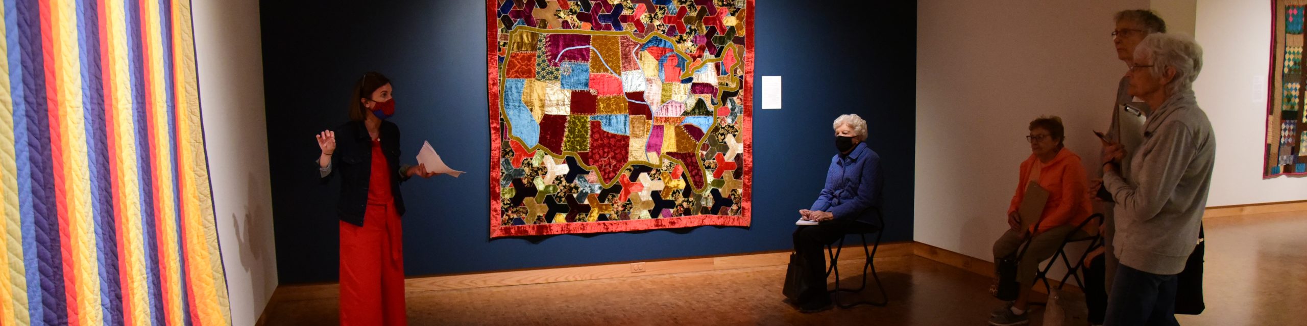 curator standing in front of quilts while 4 onlookers enjoy the explanation