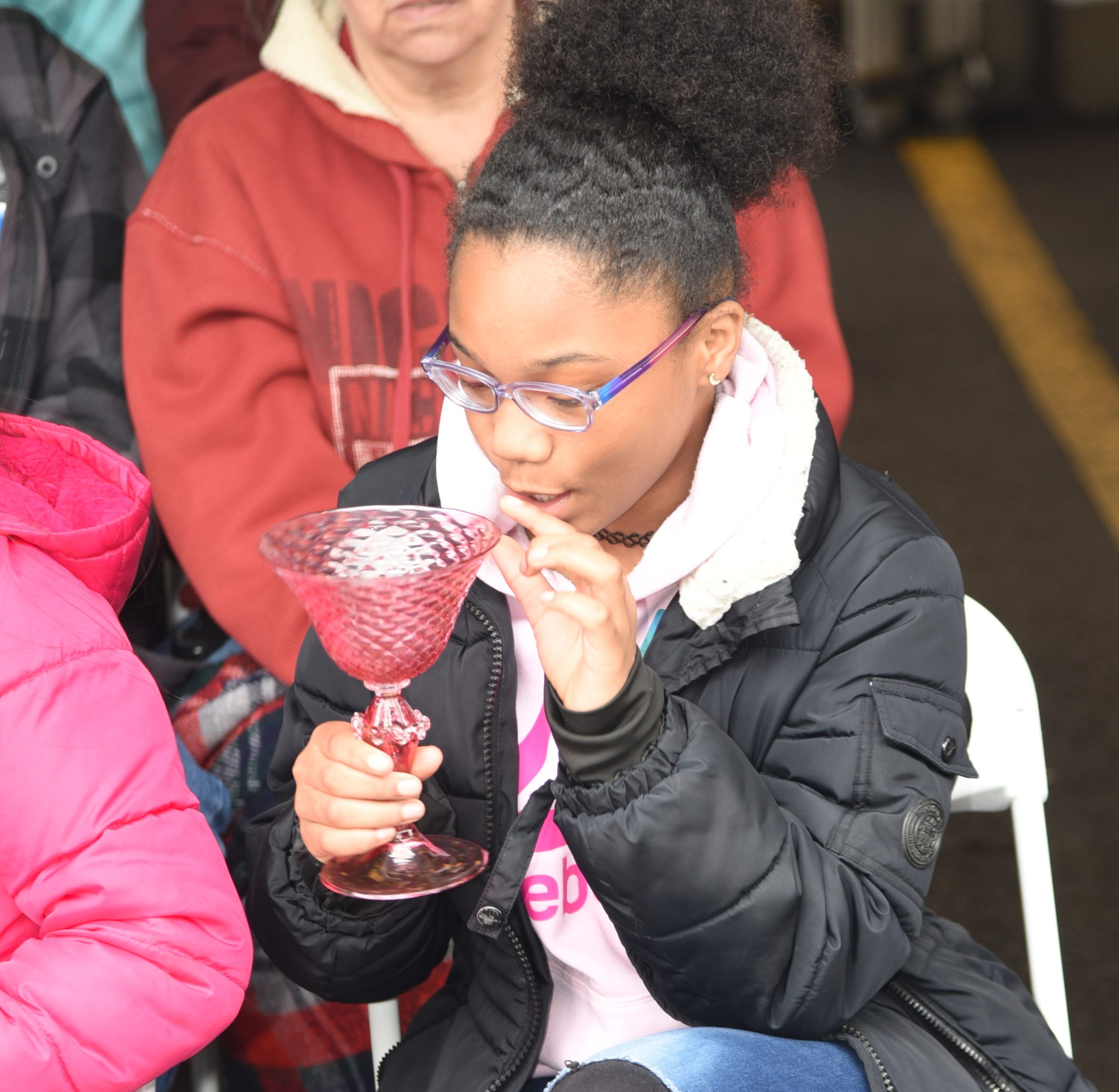 During a class visit, a student smiles as she holds a pink glass goblet created by glassmakers.