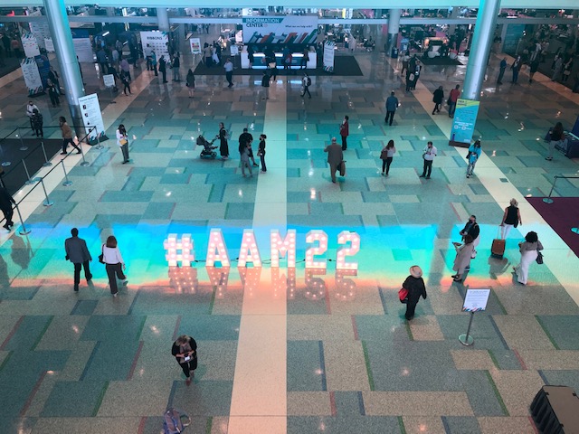 Attendees walk by a large illuminated sign featuring the 2022 American Alliance of Museum conference hashtag AAM22.