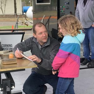 Glassmaker Eric Meek consults on the Corning Hot Shop stage with child artist about the design for You Design It; We Make It! object.