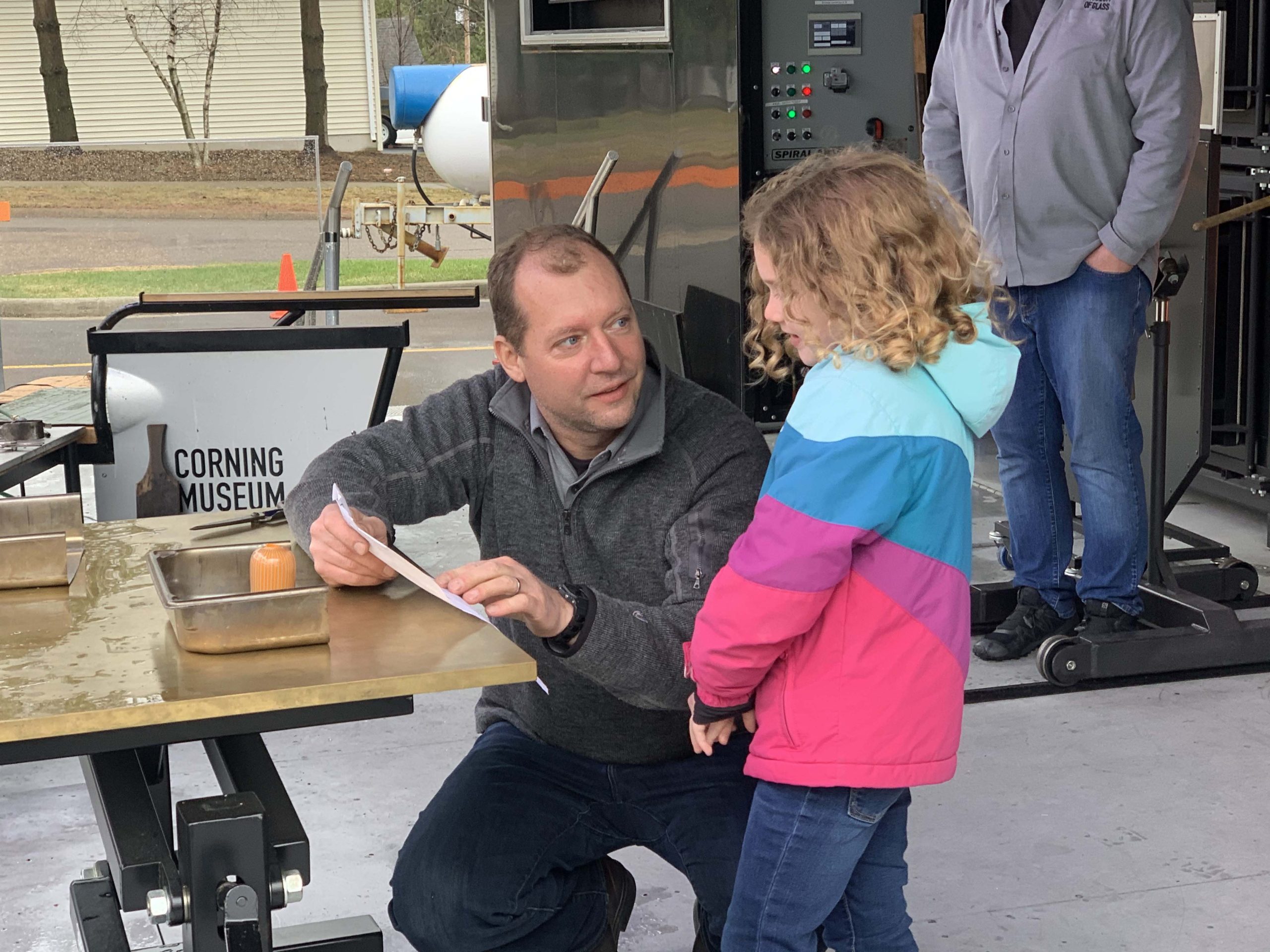 Glassmaker Eric Meek consults on the Corning Hot Shop stage with child artist about the design for You Design It; We Make It! object.