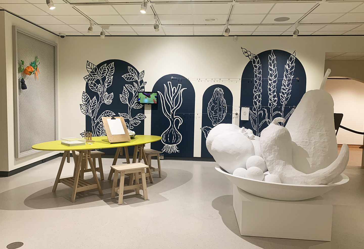 Art Park, the Museum's lower level interactive gallery is newly re-landscaped with hand-painted images of botanicals on the walls in blue and white and an oversized still life sculpture featuring an all white tomato, pear, pepper, and grapes surrounded by tables and chairs with drawing materials. 