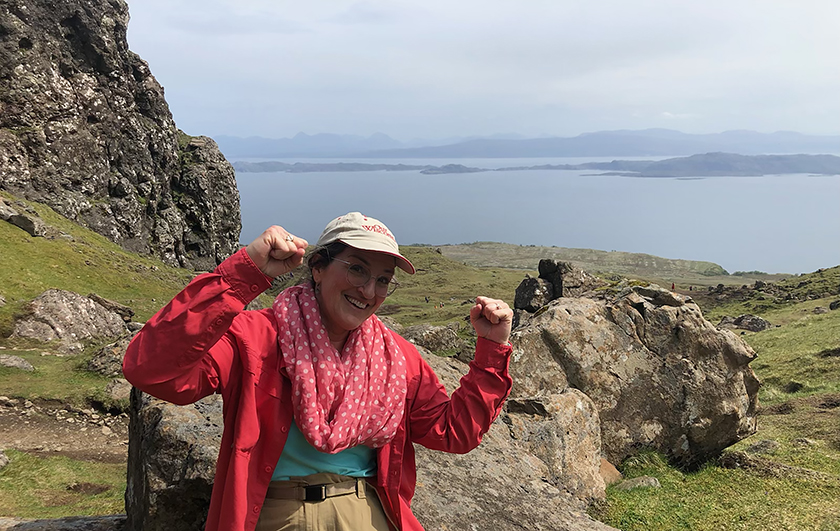 A woman smiles on a mountain with a view of western Scotland's Isle of Skye in the background. 