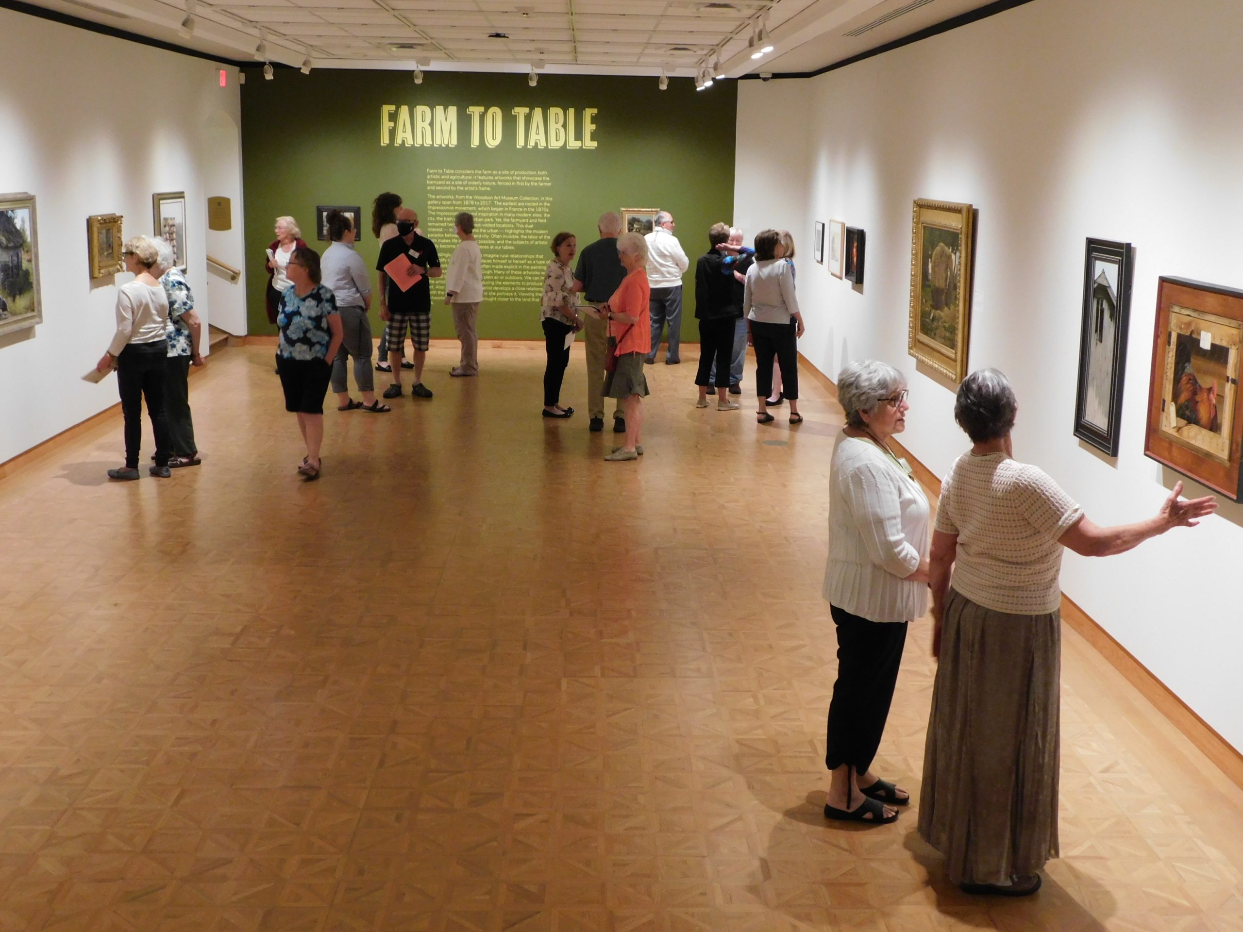 About 15 visitors stand in small groups while viewing artwork on Woodson Art Museum gallery walls.
