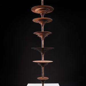 Seven wooden discs of varying sizes are arranged vertically on a wooden column, resting on a white square base
