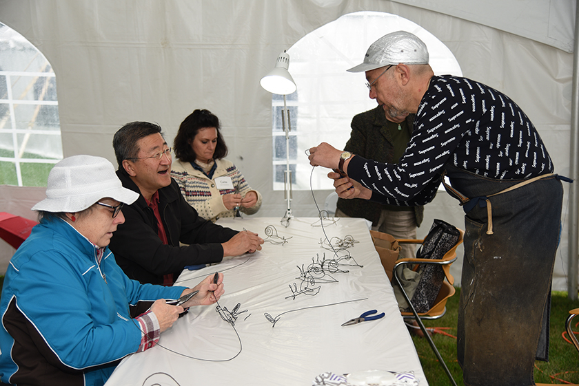 On the right, the artist Tom Hill is holding a piece of wire. On the left are three people sitting down all listening to Tom