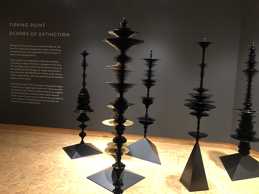 Five vertical sculptures with stacked discs resembling vinyl records are in a museum gallery.