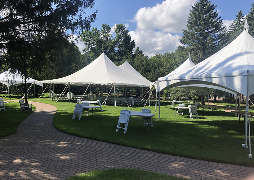 Several large white tents are set up on green grass, near a brick walkway in the Museum's sculpture garden.