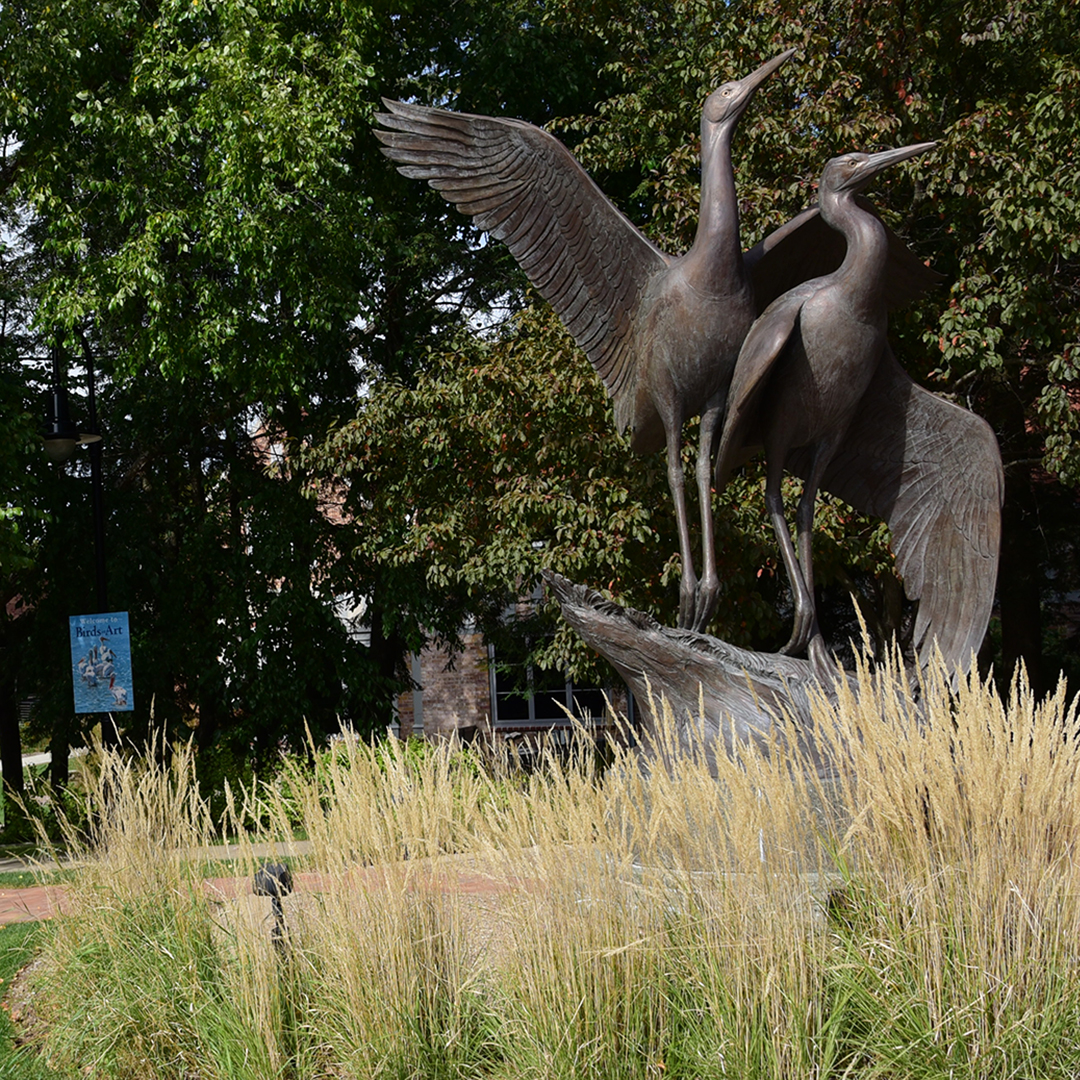 Sculpture of a whooping crane pair with a "Birds in Art" banner in the background.