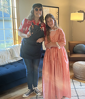 This photo shows Catie Anderson dressed as sculptor Tom Hill with hat, sunglasses, fun shoes, and holding wire next to a young girl dressed as Angelica Schuyler, in a fancy dress