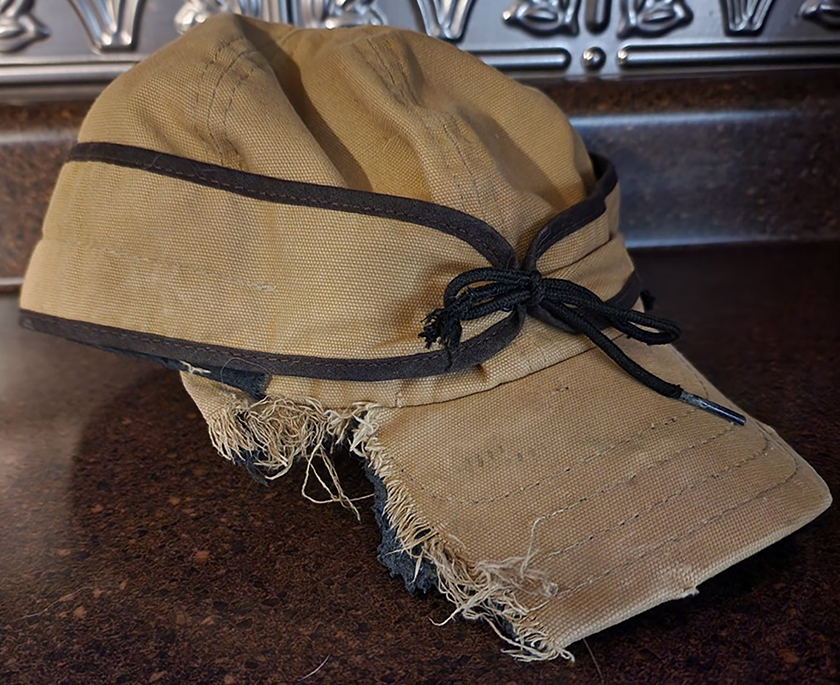 A tan Stormy Kromer cap showing a damaged bill chewed by a puppy