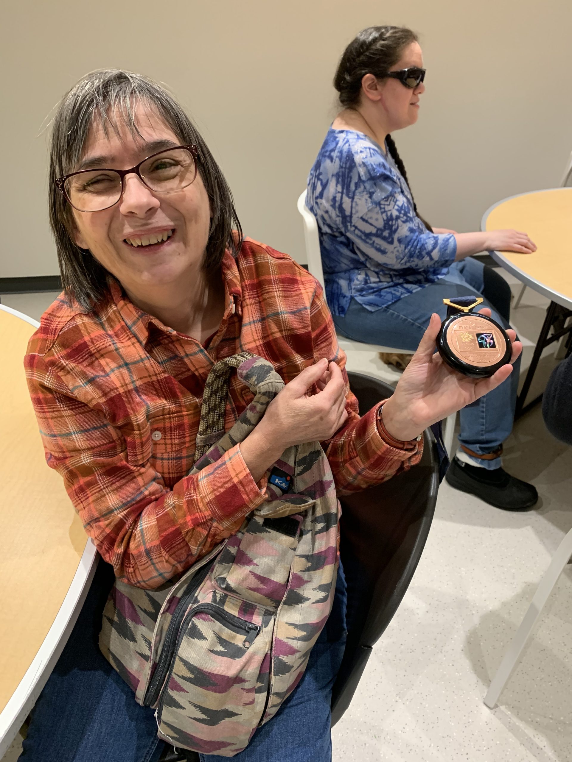 Art Beyond Sight Participant smiles for the camera and poses with Mike Martino's bronze Olympic medal.