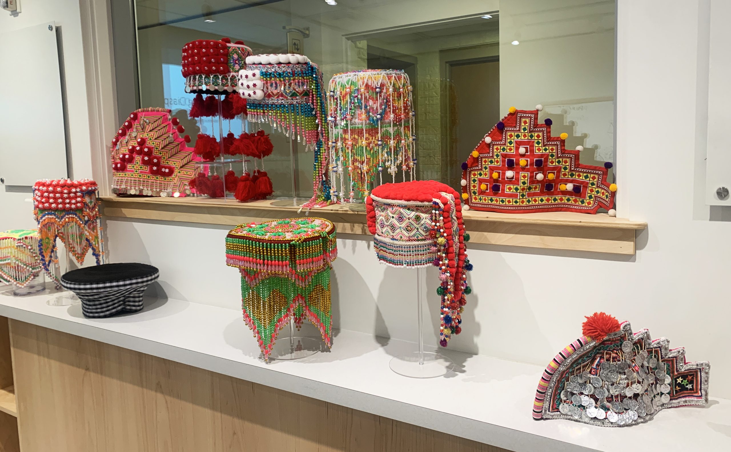 Colorful, beaded Hmong hats with pompoms, tassels, and coins sit atop a counter in the Museum's classroom space.