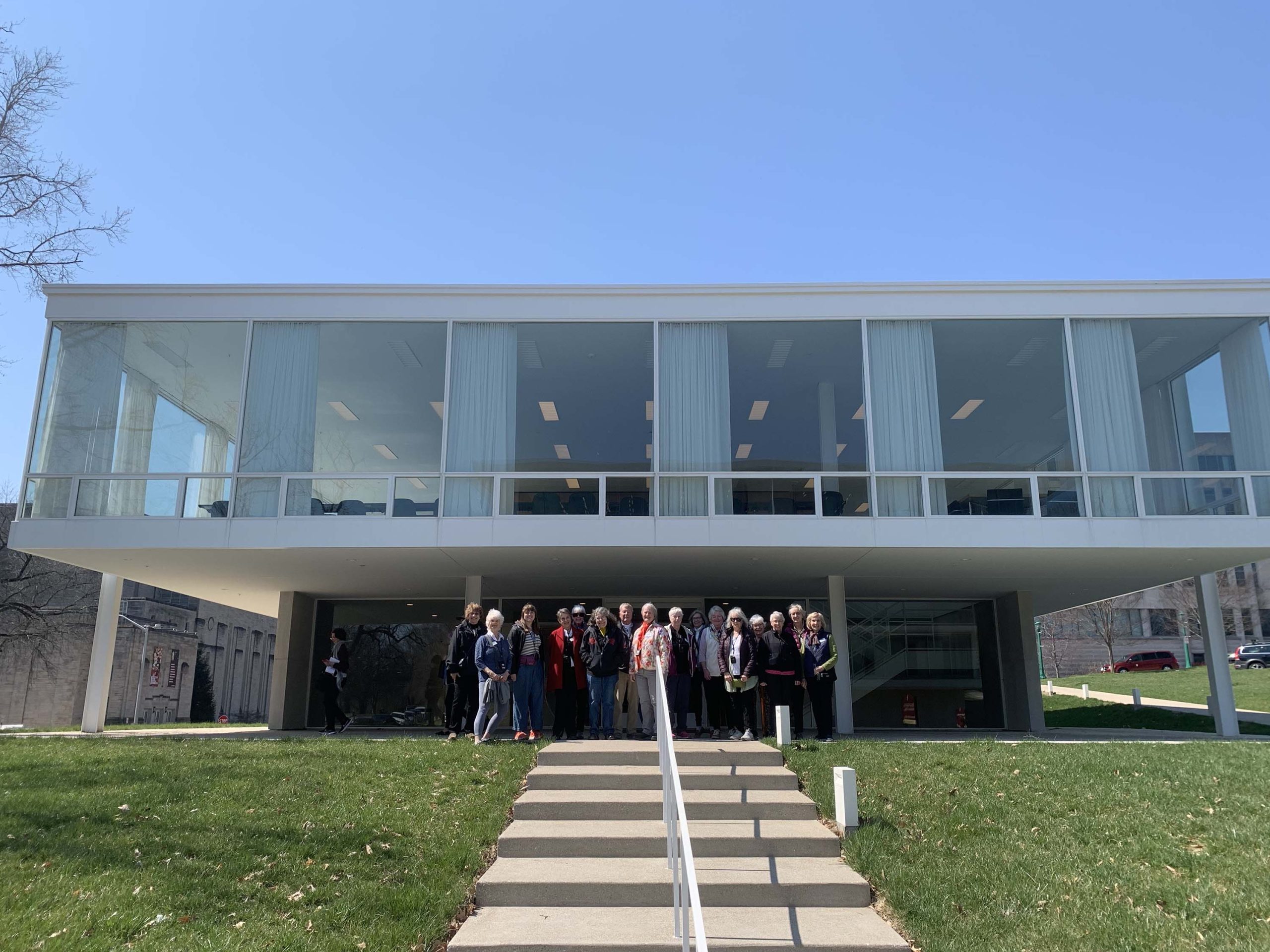 a group stands in front of a building lofted above and made of glass