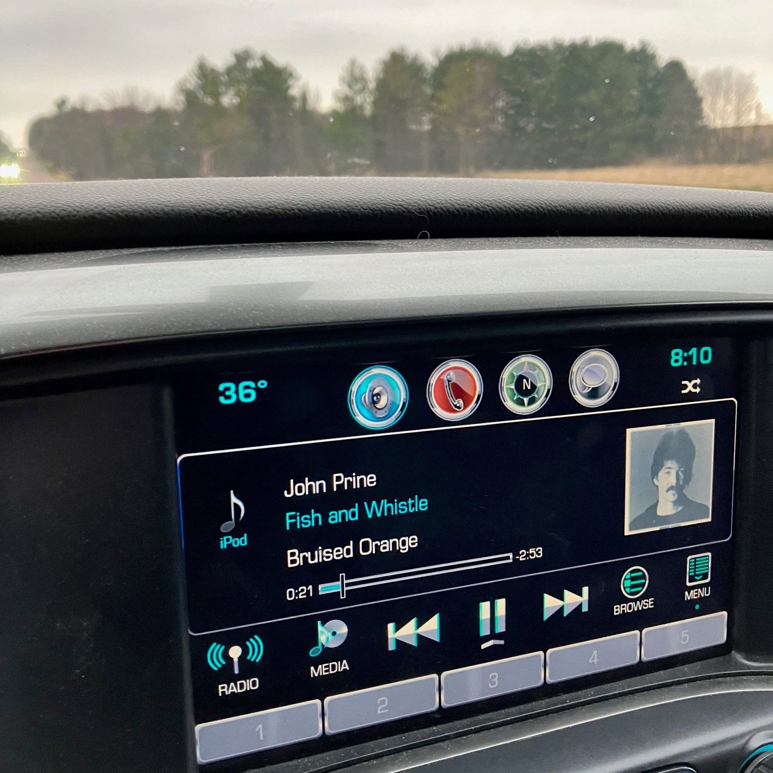 This photo shows the dashboard of a truck with a John Prine song playing