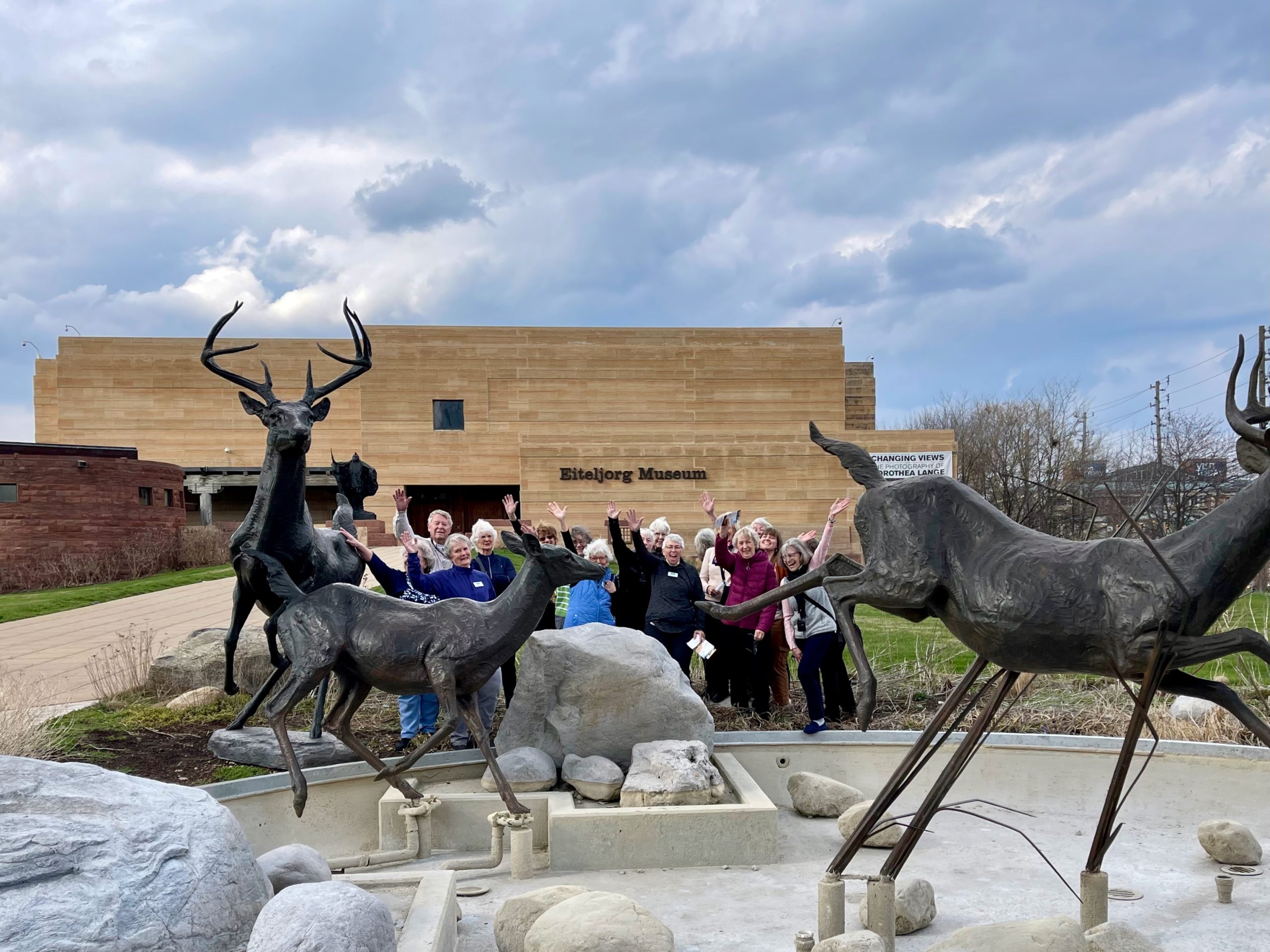 This image shows Woodson Art Museum travelers posing for a photo near large bronze deer