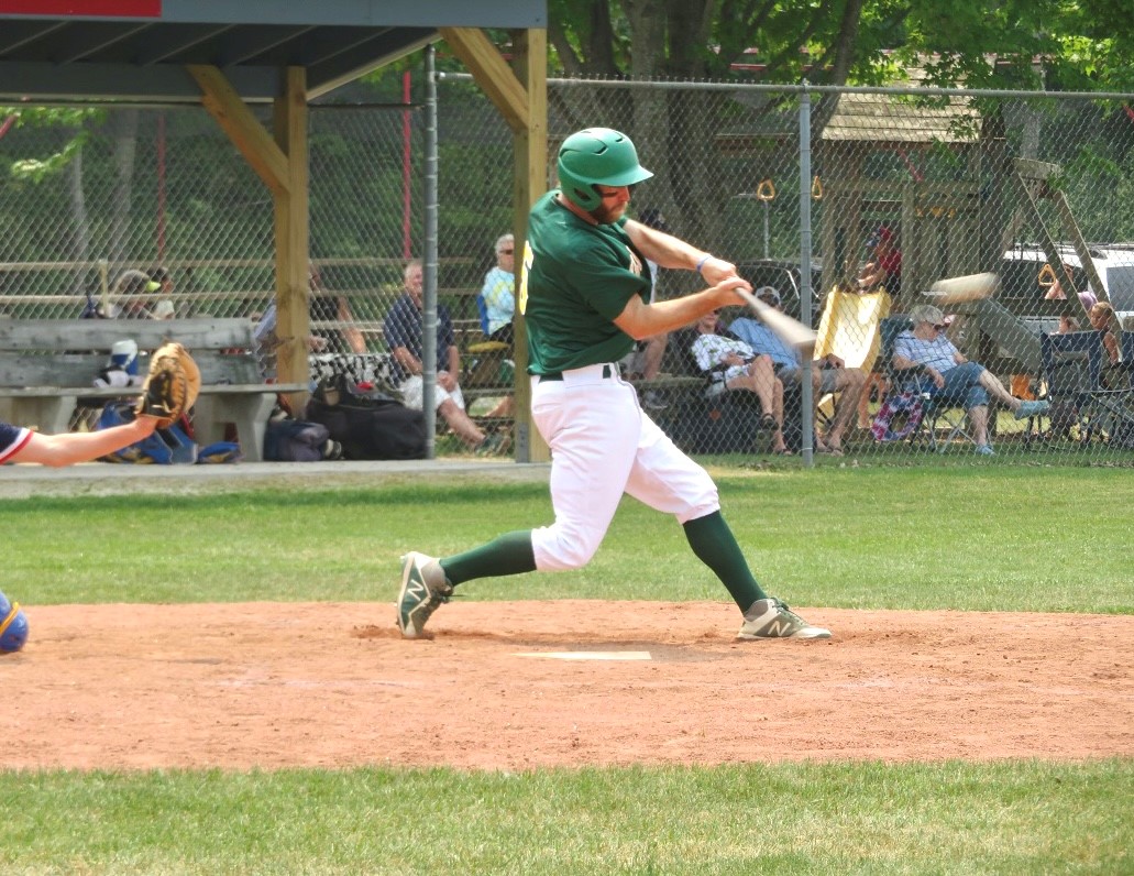 This photo shows a man in a green and white uniform hitting a baseball
