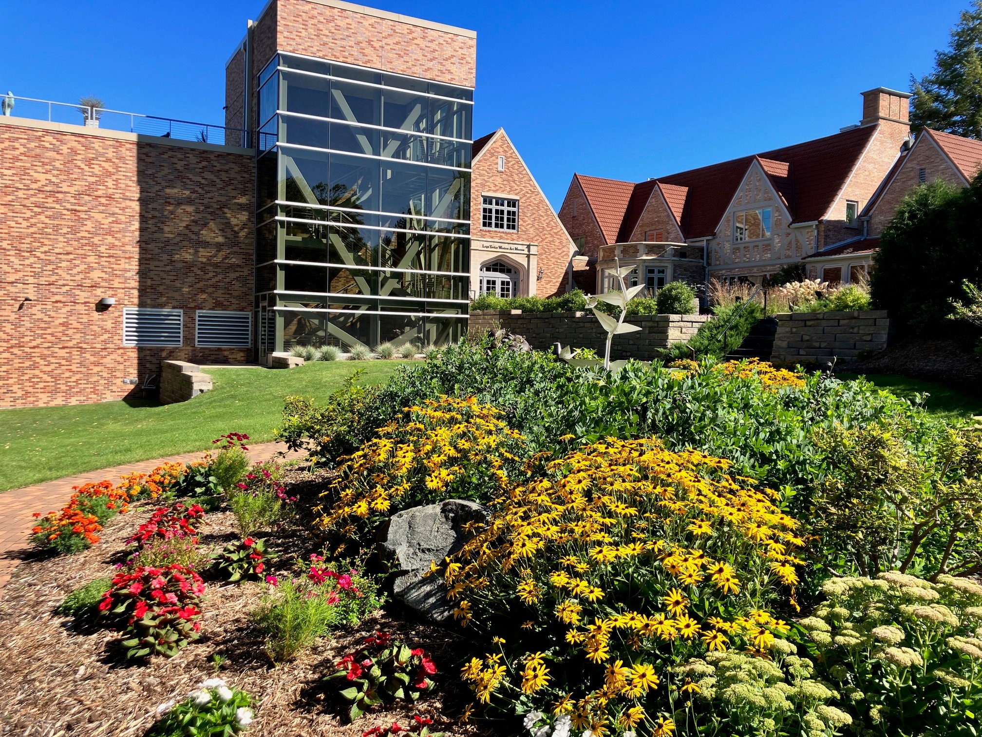 This image shows the Woodson Art Museum's grounds in full bloom with flowers in the foreground and the Museum's main entrance in the background