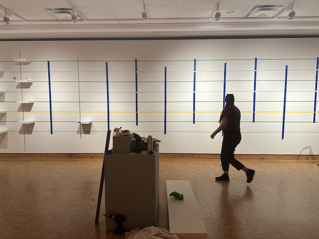 A woman walking in front of a taped off wall with shelves.