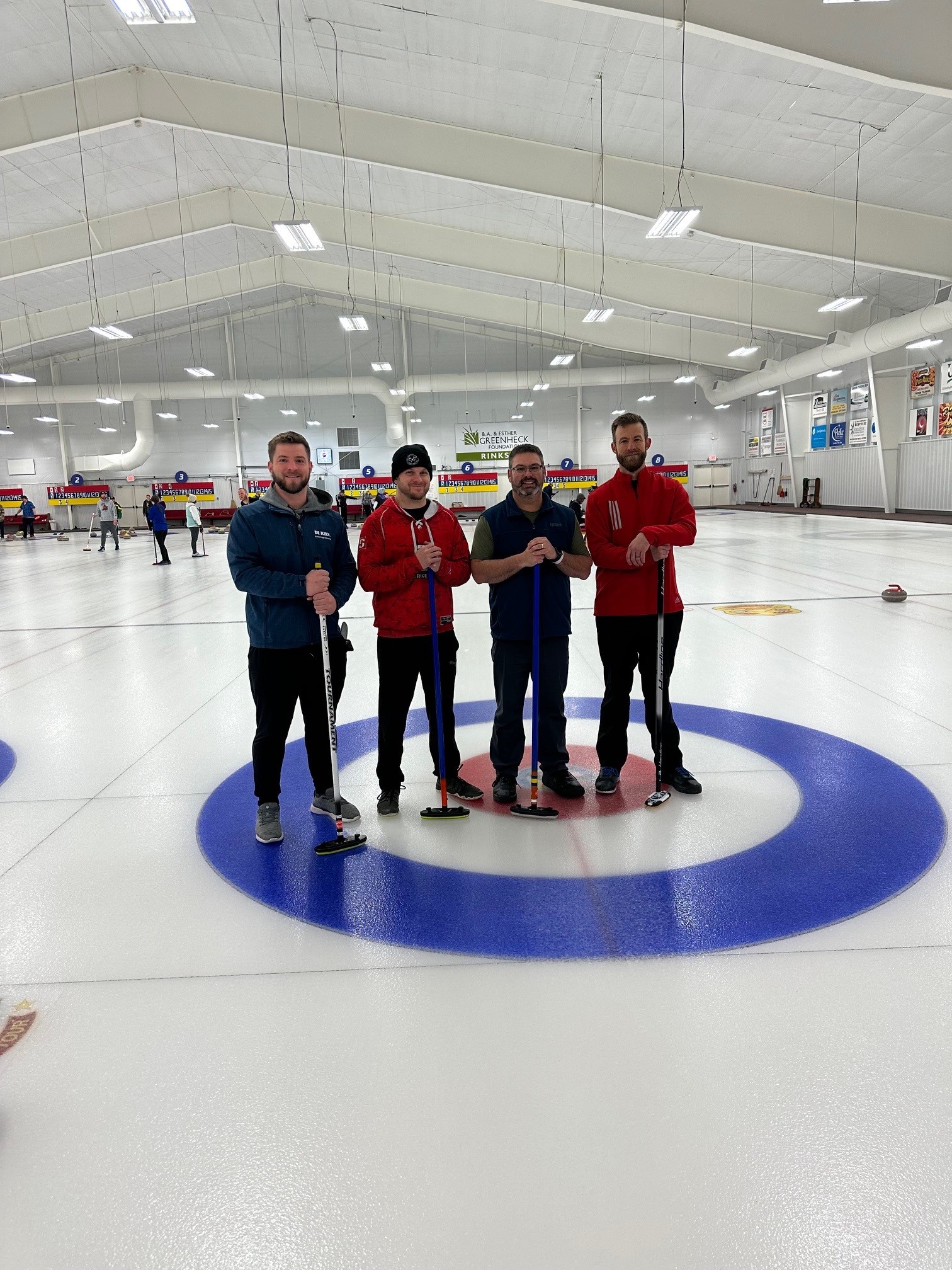 This image shows four men with curling brooms standing in the middle of a curling "house" on a sheet of ice