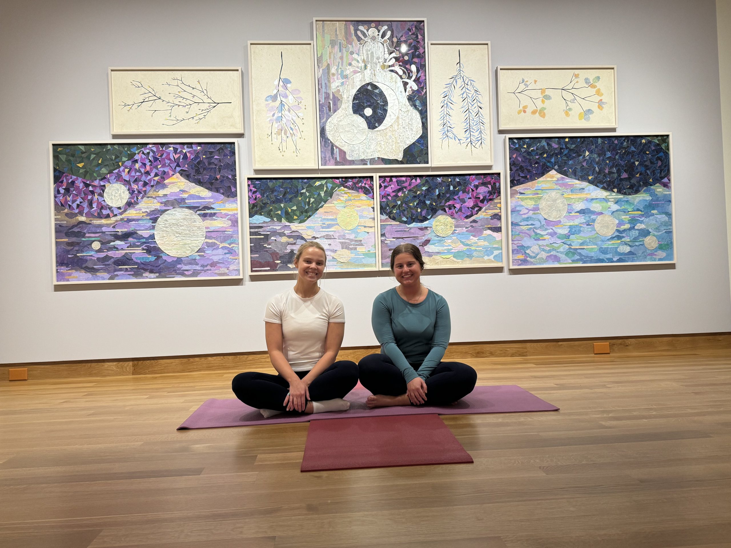 Museum staff member, Bryce, and her friend Abby sitting in front of artwork from Women Reframe American Landscape