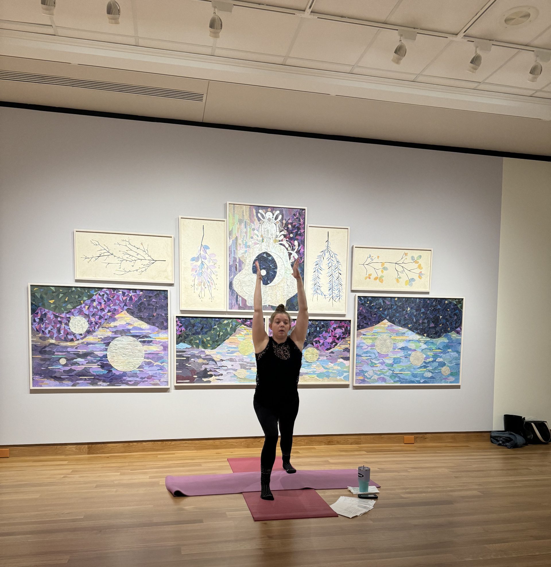 A photo of Karey, the yoga instructor, posing in a yoga position in front of artwork in the exhibition Women Reframe American Landscape