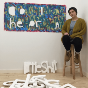 Rachel sitting next to an artwork in her studio space during the 2019 artist residency at Vermont Studio Center
