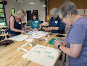 four ladies standing at a table in the glass box studio working on their handmade linocut prints during their party.