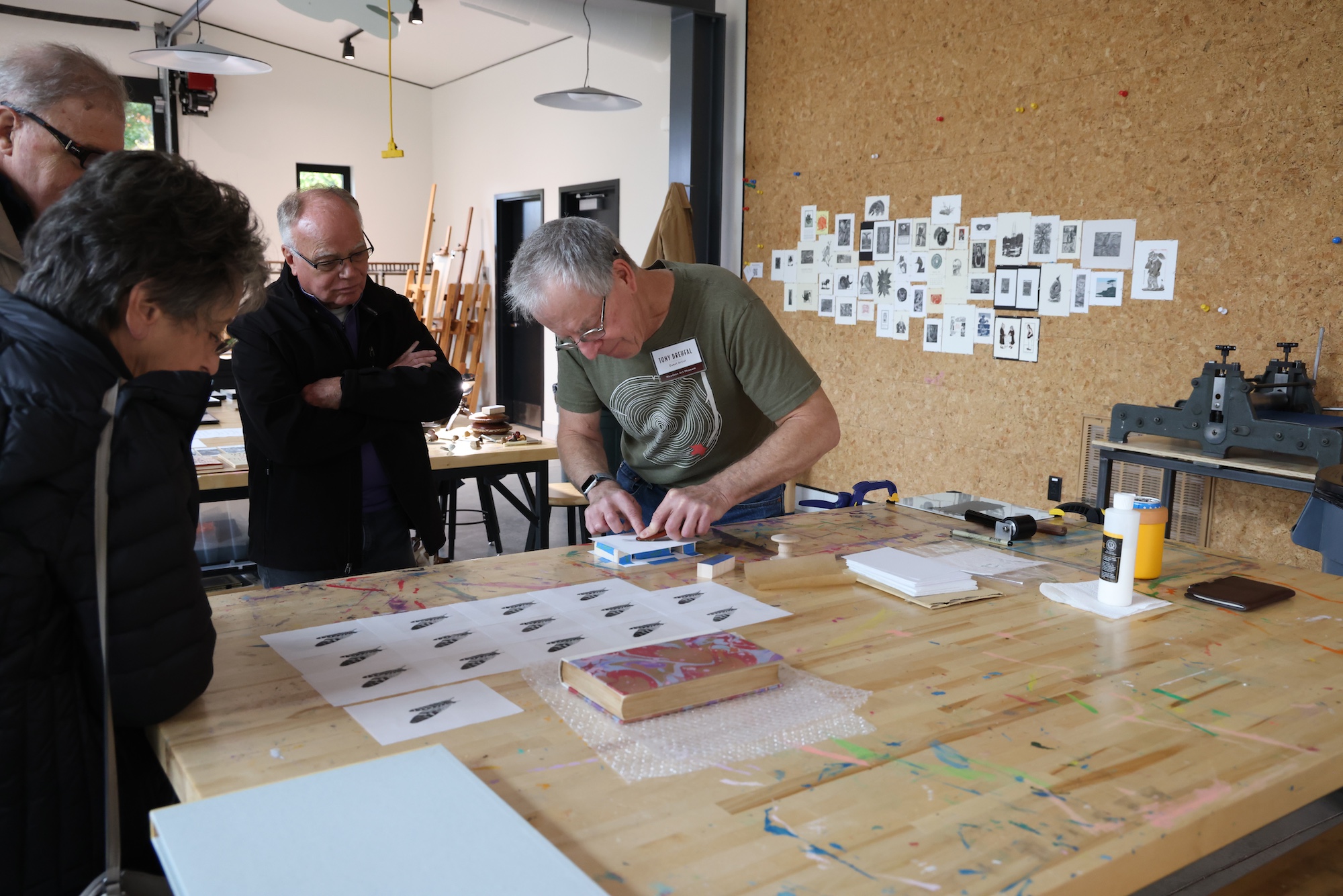 Tony standing alongside a table, working on a print while visitors watch his process