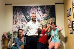 The Foss family posing for a photo in front of a backdrop created for Pao Houa Her's exhibition over the summer