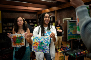 Two peolple hold coloroful artworks that they made.