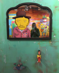 A mirror sits on a teal wall in it is a woman taking the photo and figures